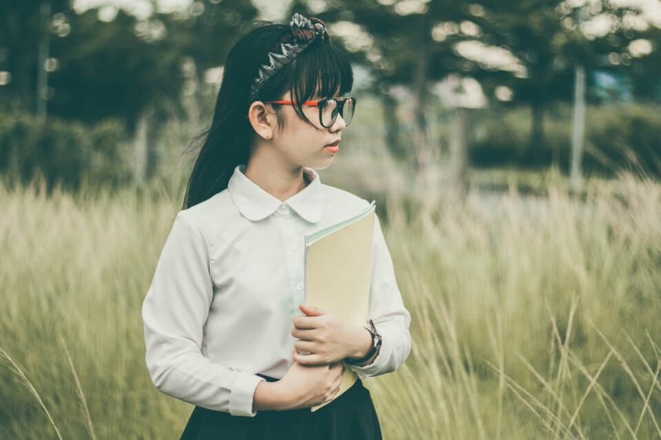 Adolescente à lunettes tenant un classeur contre elle, dans les herbes hautes