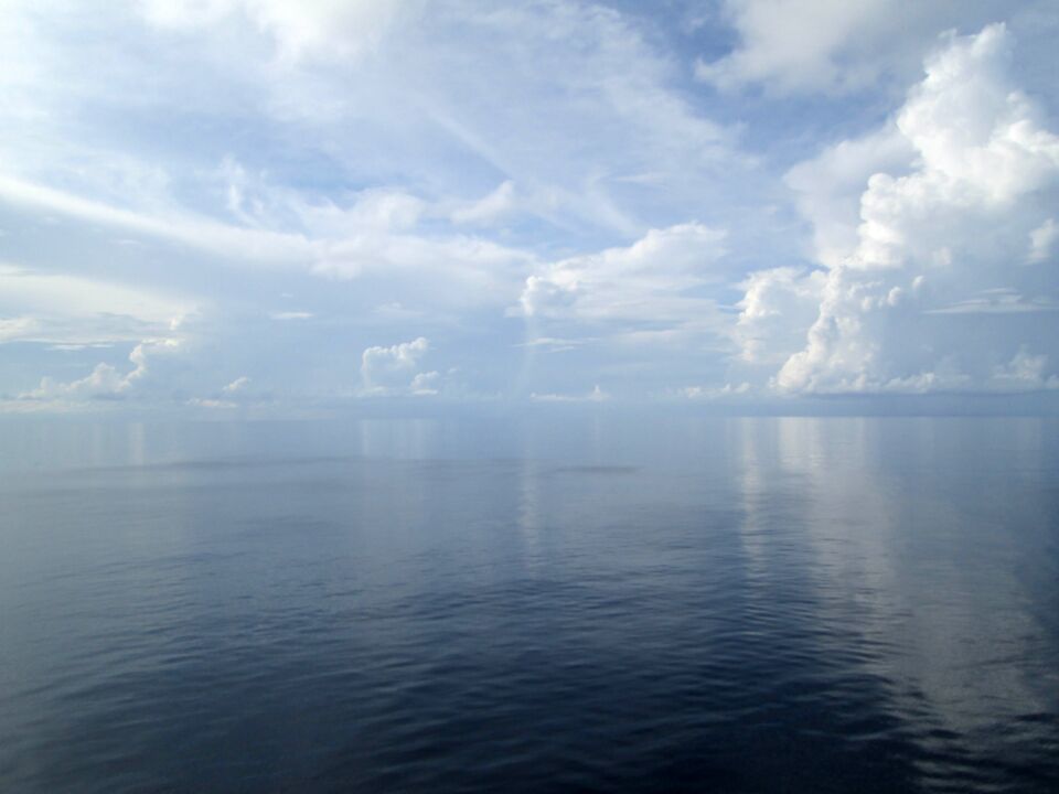 Mer d’huile sous un ciel de nuages blancs, l’horizon qui se fond dans la brume