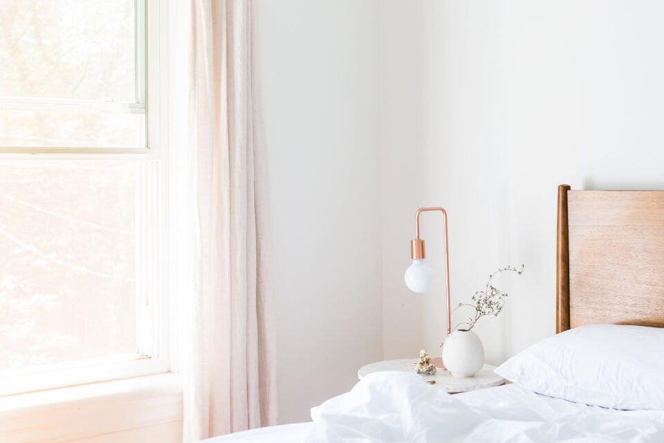 Chambre lumineuse, lit aux draps blancs, lampe cuivrée et petit vase sur la table de chevet