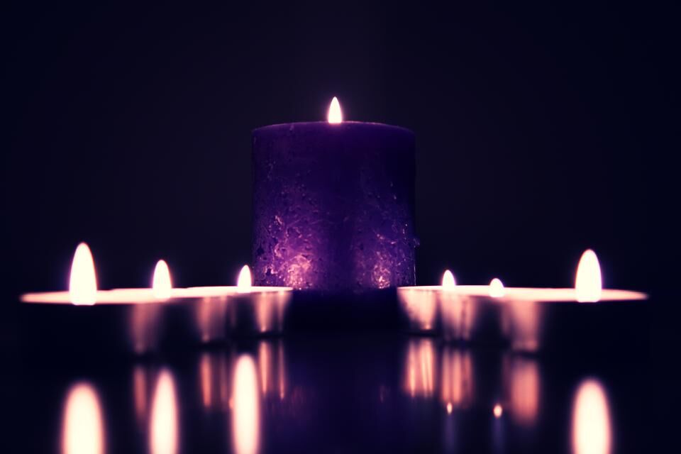 Photo d’illustration : bougie violette et petites bougies allumées, reflets sur une surface sombre