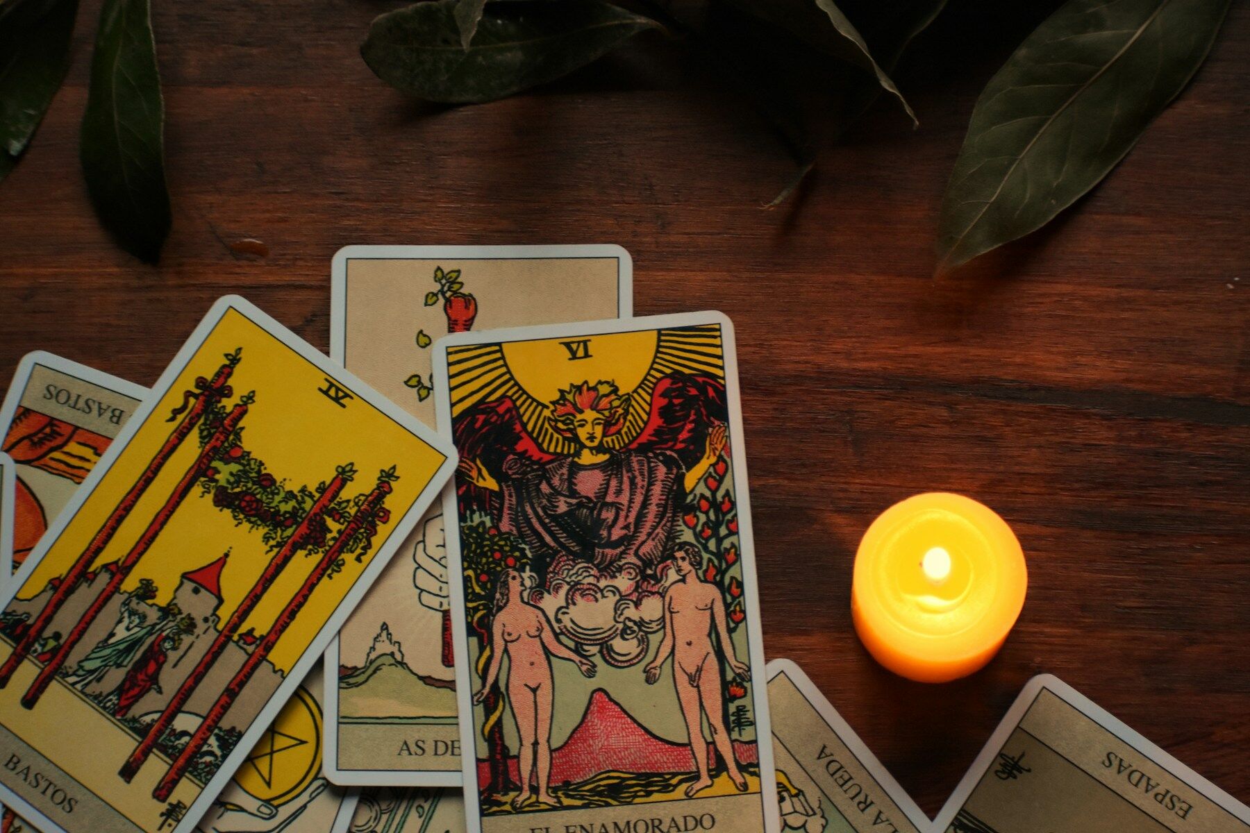 Cartes de tarot étalées sur une table en bois sombre, à côté d’une bougie allumée