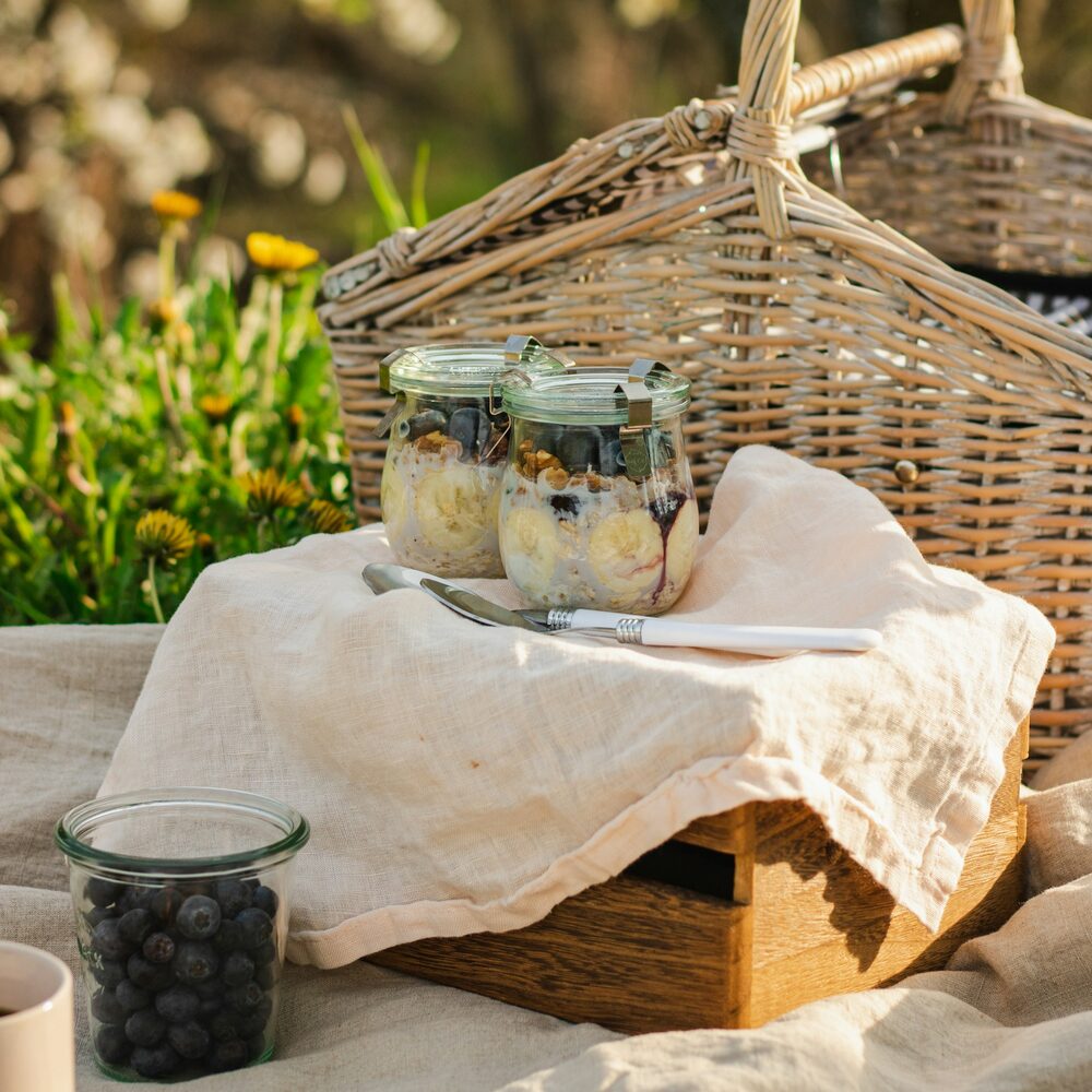 Grand panier en osier, bocaux et linge de lin posés dans l’herbe