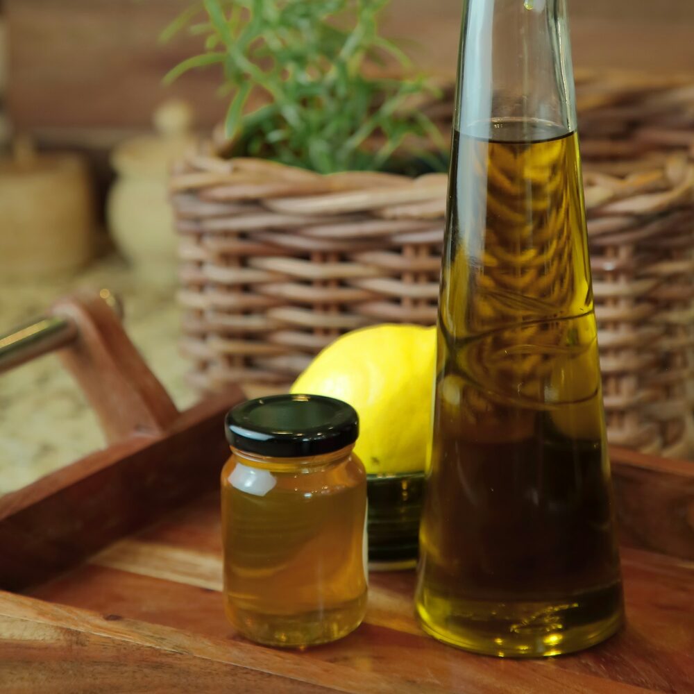 Bouteille d’huile, pot de miel, citron et romarin sur un plateau devant un panier en osier