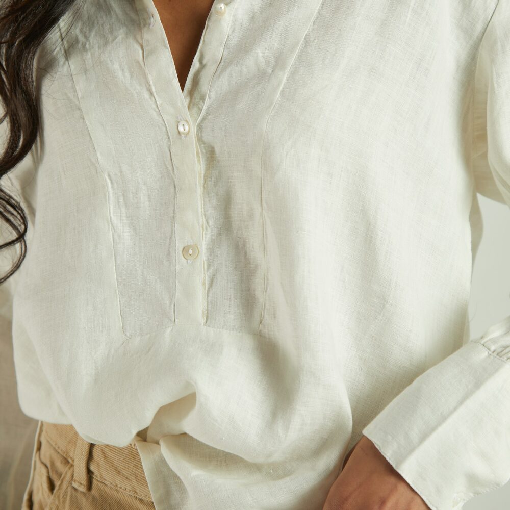 Chemise en lin écru portée ouverte au col, rentrée dans un pantalon sable