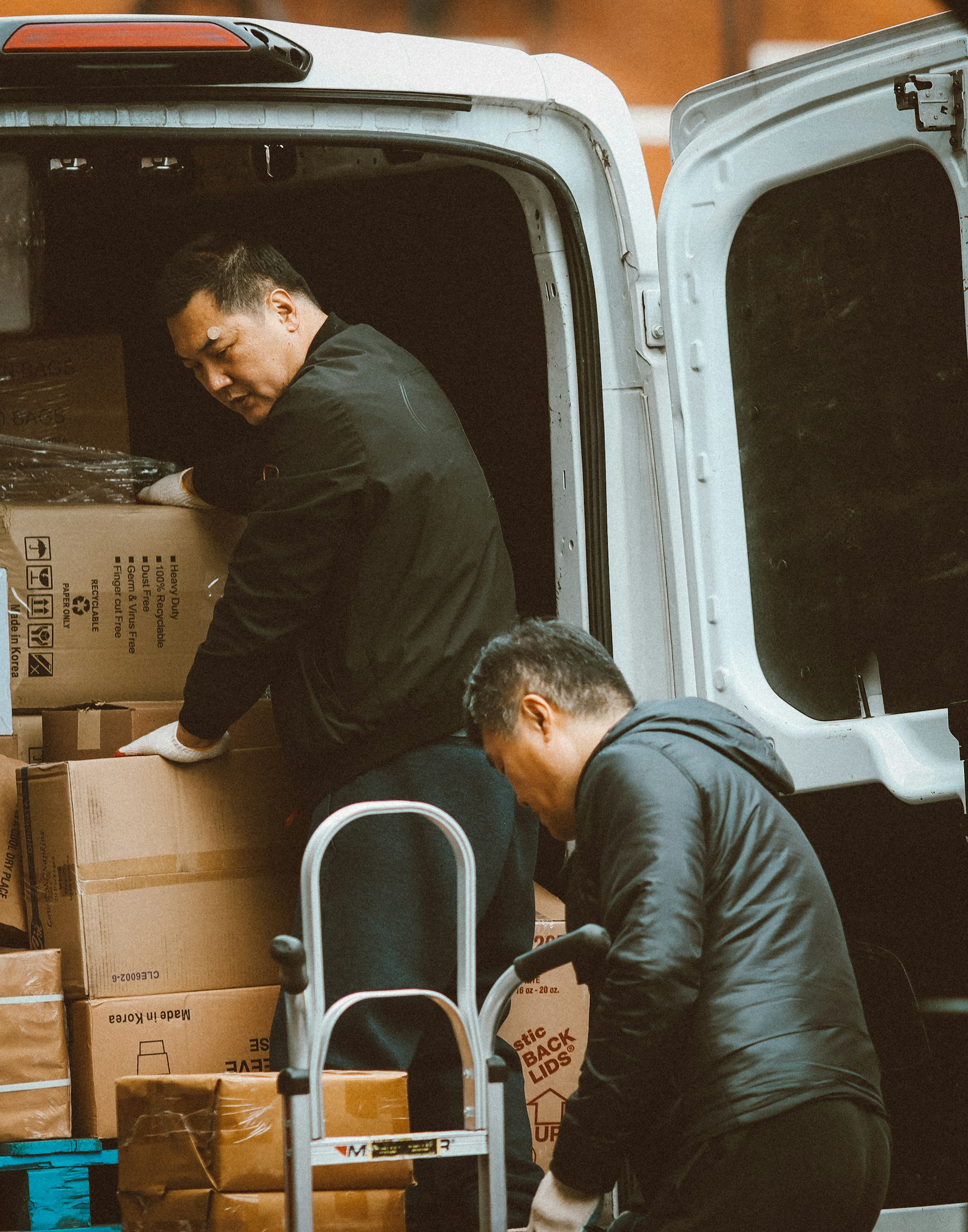 Deux déménageurs chargent des cartons dans un utilitaire, diable à côté