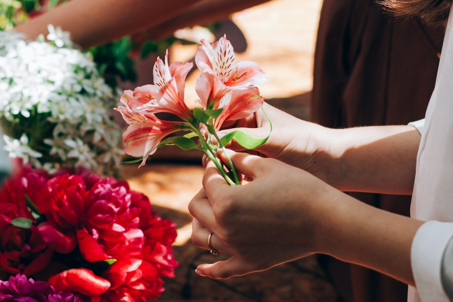 Mains qui montent un bouquet d’alstroemères, pivoines rouges et ciseaux sur l’établi