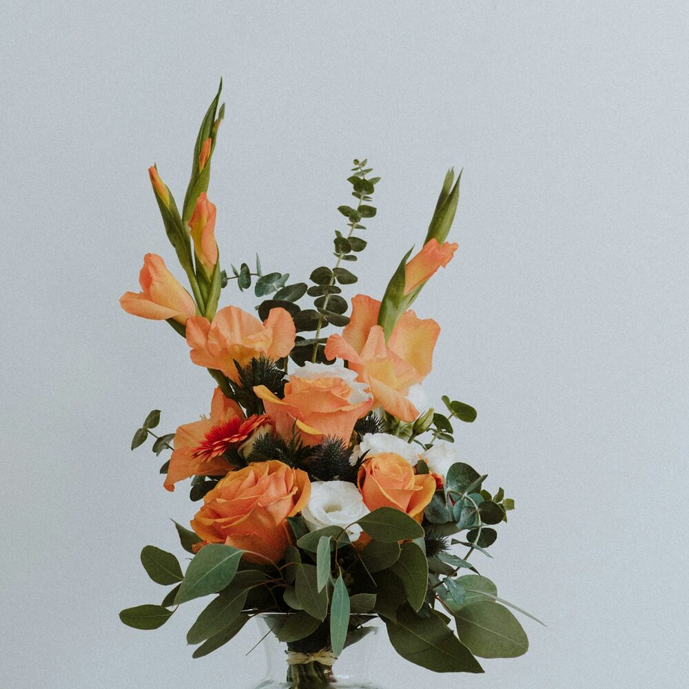 Glaïeuls et roses orange dans un vase, sur fond clair
