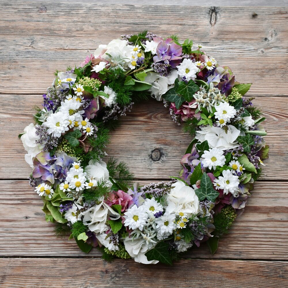 Couronne de fleurs blanches et mauves posée sur un plancher en bois