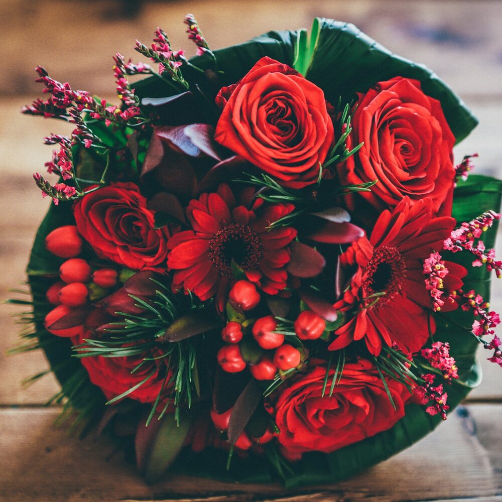 Bouquet rond de roses rouges, gerberas et baies rouges sur une table en bois