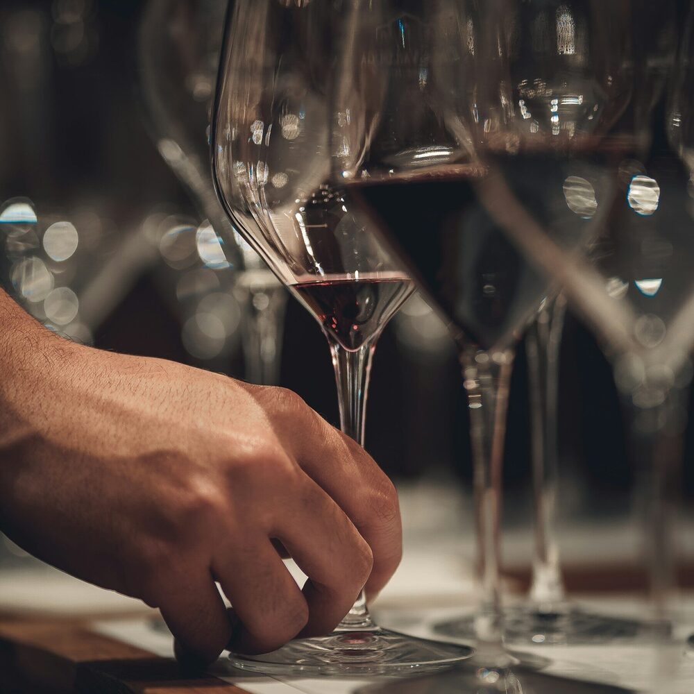 Main posant un verre de vin rouge parmi des verres alignés