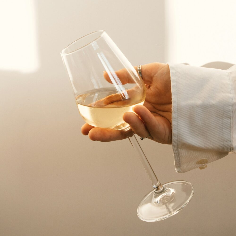 Main tenant un verre de vin blanc devant un mur clair
