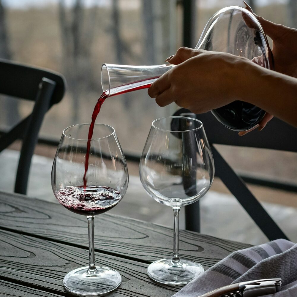 Vin rouge versé d'une carafe dans un verre, sur une table en bois