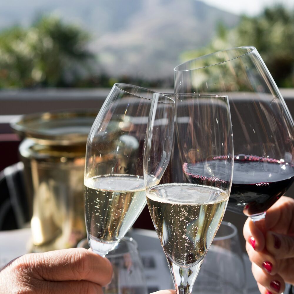 Deux flûtes de vin effervescent et un verre de rouge qui trinquent en terrasse