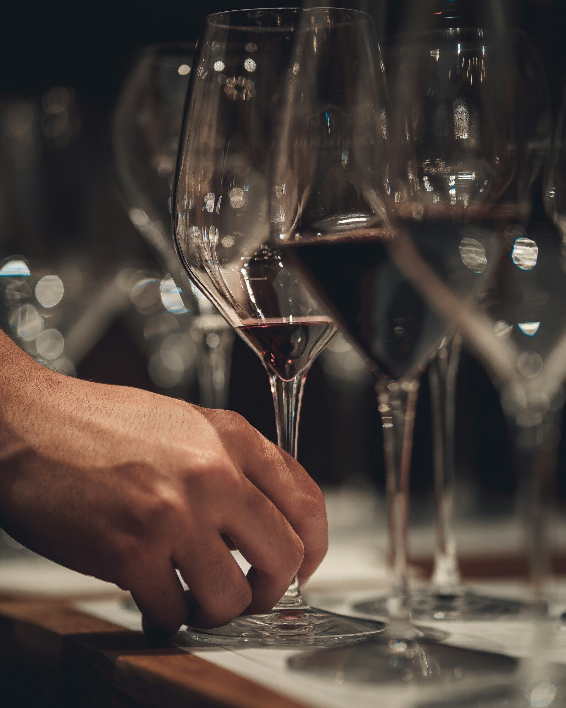 Main posant un verre de vin rouge parmi des verres alignés