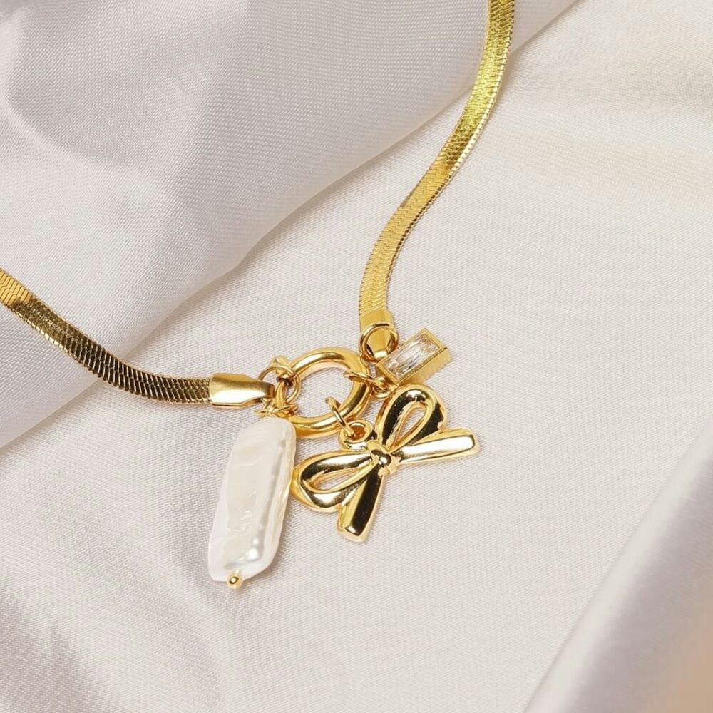 Chaîne serpent dorée avec breloques nœud et perle sur satin blanc