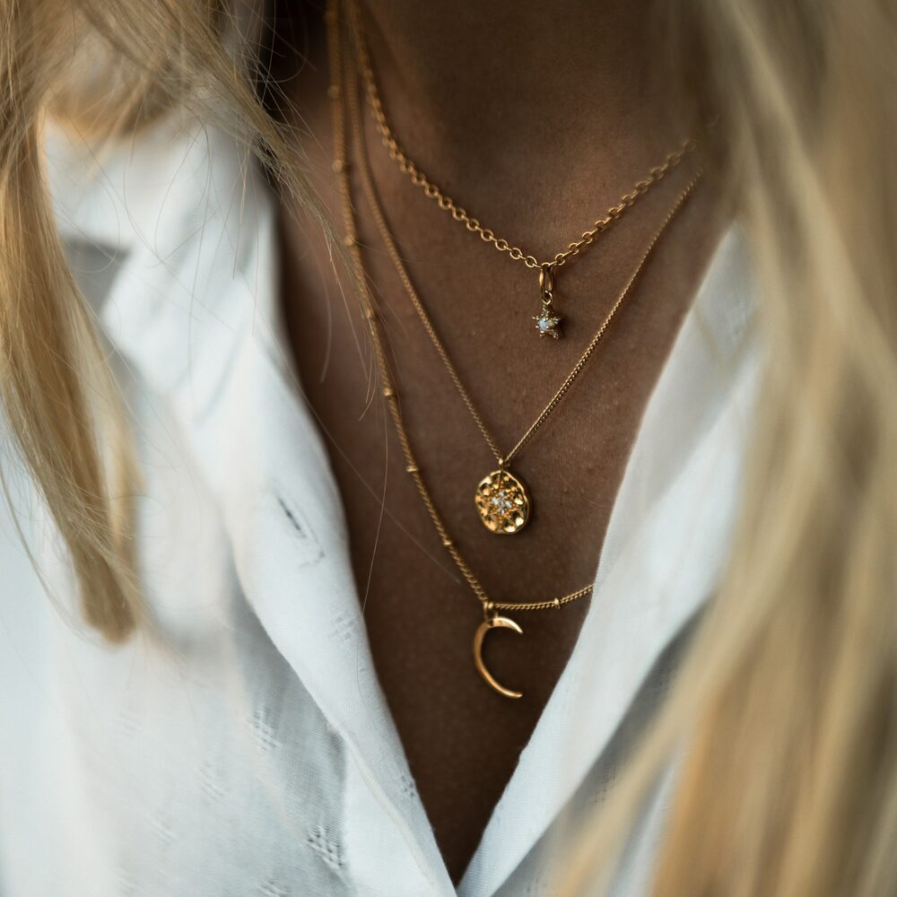 Trois colliers fins dorés superposés sur une chemise blanche