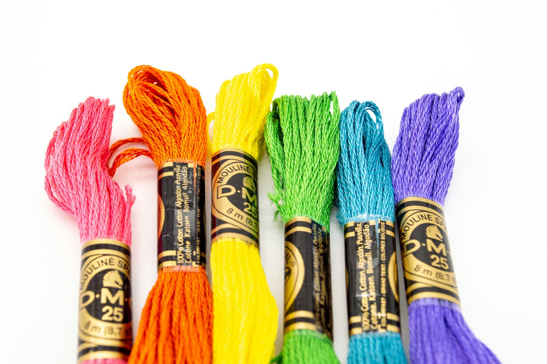 Écheveaux de fil à broder rose, orange, jaune, vert et bleu alignés