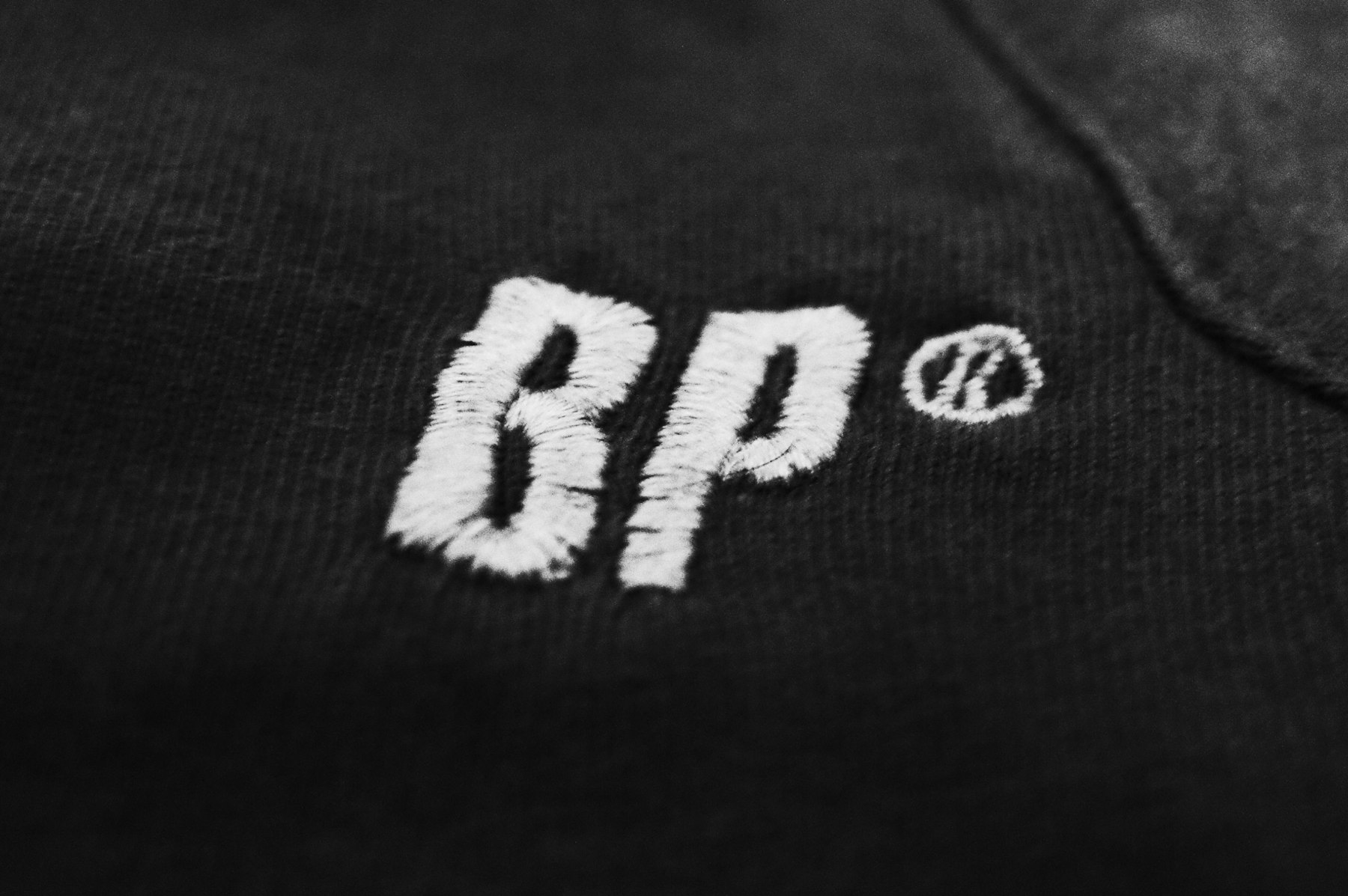 Logo brodé en fil blanc sur un textile bleu foncé, vu de très près