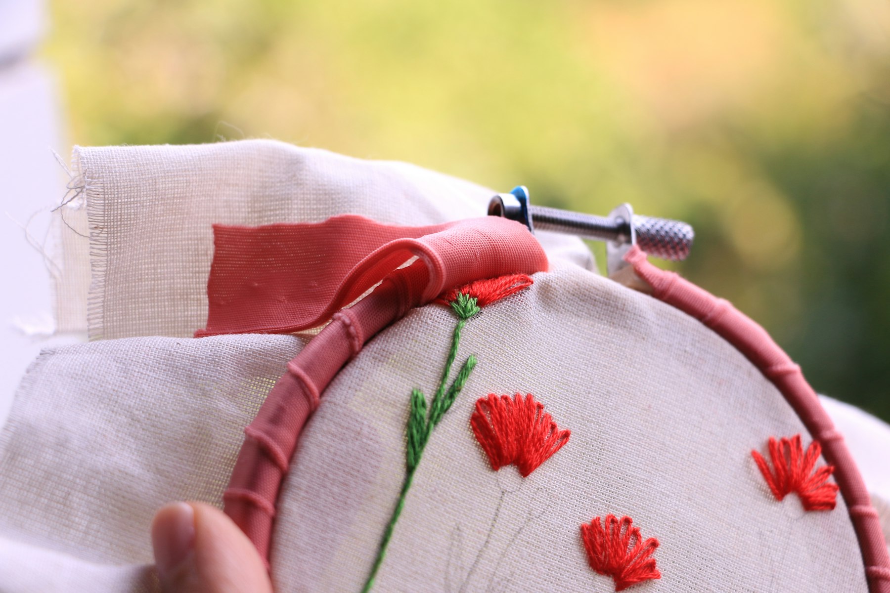 Mains tenant un tambour à broder en bois, coquelicots brodés en fil rouge sur un tissu blanc
