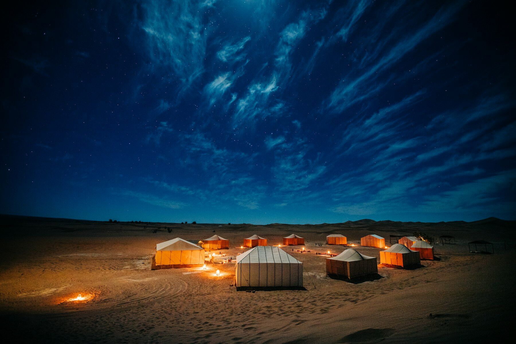 Bivouac illuminé de nuit dans les dunes sous un ciel bleu profond