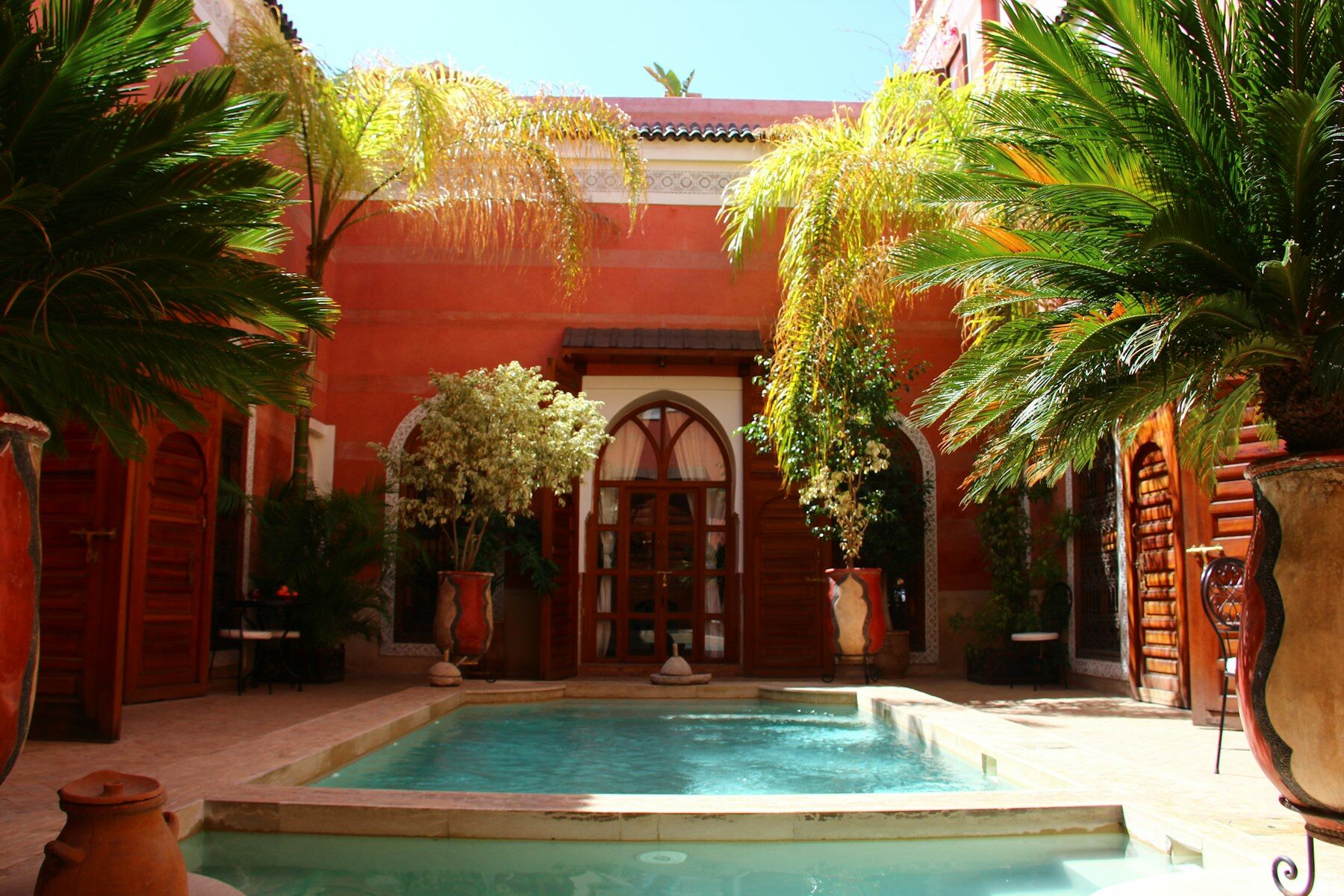 Patio de riad aux murs ocre rouge, bassin turquoise et palmiers