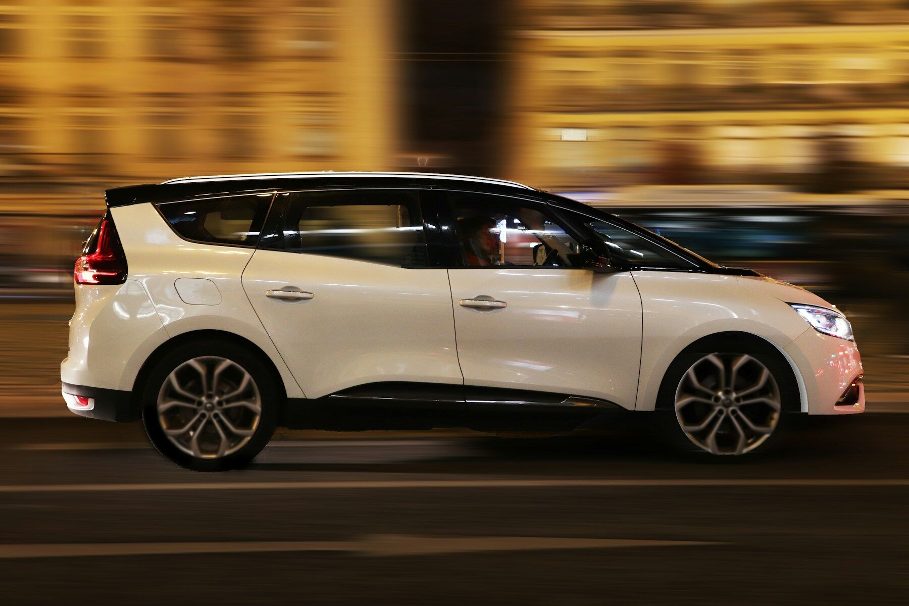 Monospace blanc roulant le soir dans une rue éclairée